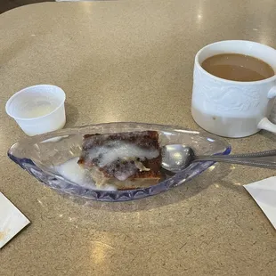 Bread pudding with sauce served on the side with a hot cup of coffee .