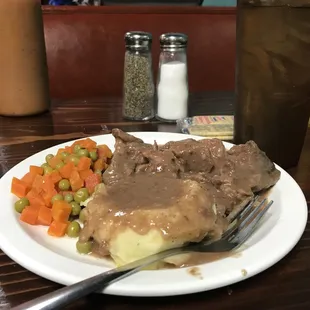 a plate of food with gravy, mashed potatoes, carrots and peas