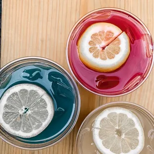 three glasses of different colored liquid with a slice of lemon