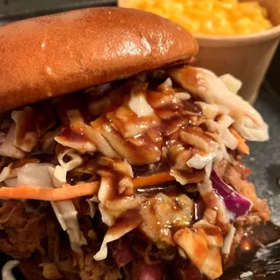 Pulled pork sandwich with coleslaw on top. Mac n cheese on the side.