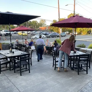 people walking around a patio with tables and umbrellas