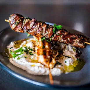 a meat skewer on a bed of mashed potatoes