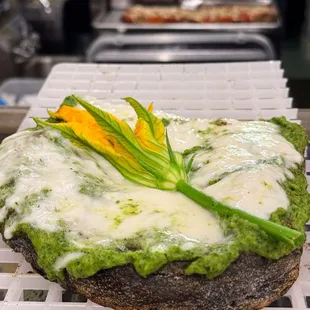 Activated charcoal, rye, sourdough, rice, &amp; soy flour crust. Zucchini + arugula pesto sauce topped w/ stracciatella &amp; zucchini flower