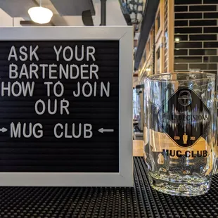 a glass of beer and a sign that says ask your bartender how to join our mug club