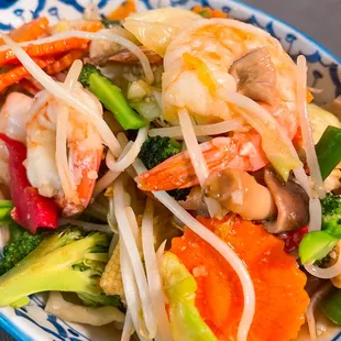 a blue and white plate with shrimp, broccoli, carrots, and noodles