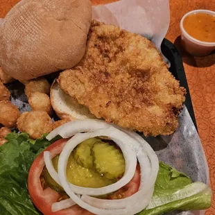 a chicken sandwich with lettuce, tomato, onion, and pickle