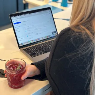 a woman sitting at a table with a laptop and a drink