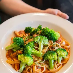 a person holding a plate of pasta and broccoli