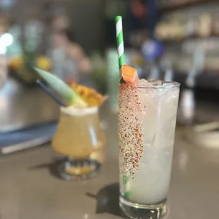 a glass of cocktail with a straw and garnish garnish