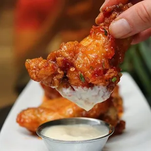 a hand dipping a piece of chicken wings
