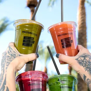 a hand holding three cups of smoothie