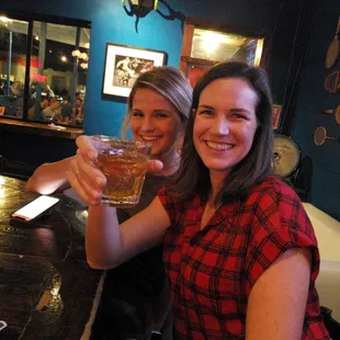two women sitting at a bar, one holding a glass of beer