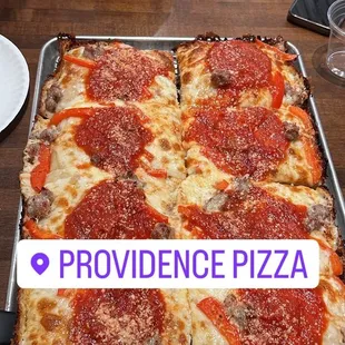 Detroit style pizza 12x18. Topped with red sauce, red peppers, Italian sausage, hot honey, mozzarella, and Asiago cheese.