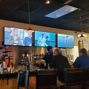 people sitting at a bar watching tvs
