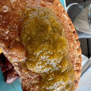 Beef Empanada doused in their amazing homemade hot sauce!  So crispy &amp; delicious it will blow your mind