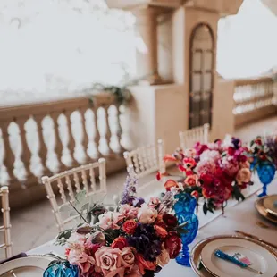 Another gorgeous tablescape!   Gold chiavari chairs, gold rimmed plates, gold flatware, colored glassware, &amp; charger plates.