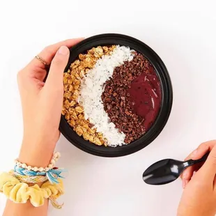 two hands holding a spoon and a bowl of smoothie