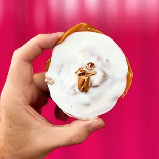 a hand holding a donut with icing and nuts
