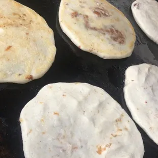  several pupusas cooking on a grill