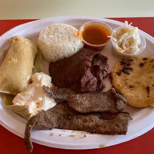 Combination plate with rice, beans, steak, cream, tamale, and pupusas