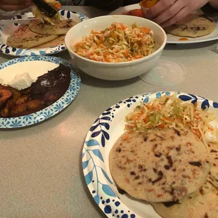 2 papusas, vegetable toppings (ensalada picante), and fried plantains (with crema, beans, and cheese)