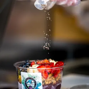 a person sprinkling sugar over a bowl of fruit