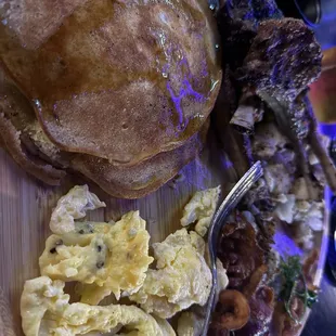 Lamb chops with home fries, scrambled eggs, and pancakes.