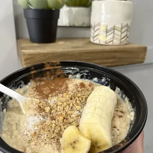a hand holding a bowl of oatmeal with bananas and granola