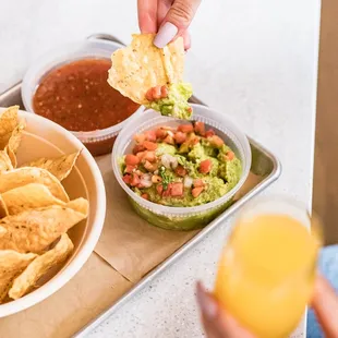 a person dipping a tortilla into a bowl of guacamole