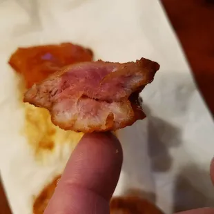 a hand holding a piece of bacon