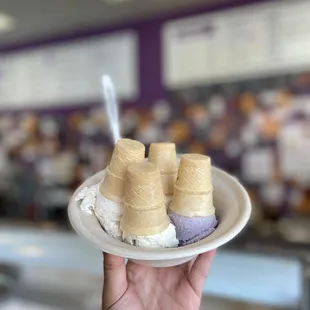 a hand holding a plate of ice cream cones