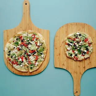 two pizzas on wooden paddles
