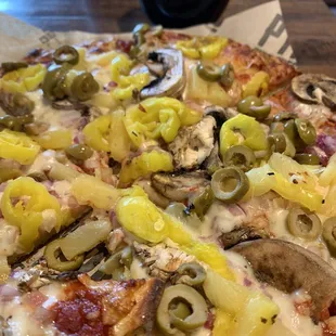 Pizza with red onions, mushrooms, pineapple, banana peppers, green olives. Glass of Pinot noir poking its head up in the background.