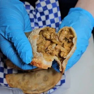 a person in blue gloves holding a piece of empanada