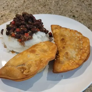 two empanadas on a plate with rice and beans