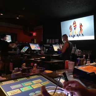 a bartender at a bar in front of a large screen