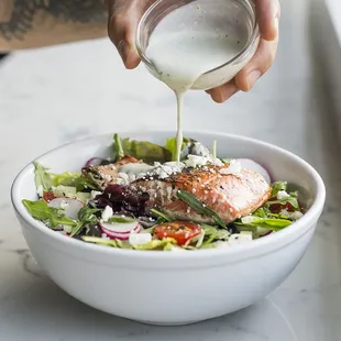 a person pouring dressing over a salad