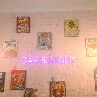 a woman sitting at a table in front of a brick wall with a neon sign that says day and night