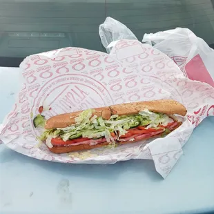 a sub sandwich on a wrapper on the hood of a car