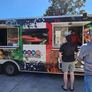two people standing in front of a food truck