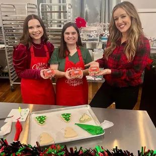 three women in aprons holding christmas cookies