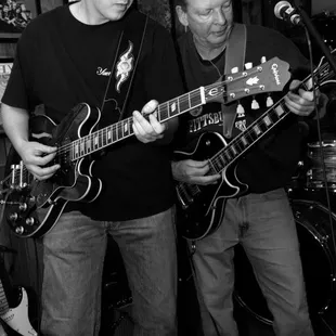 two men playing guitars in a bar