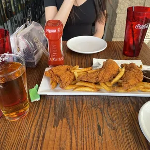  a woman sitting at a table with a plate of fried chicken and fries