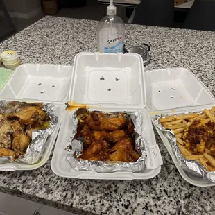 three takeout containers of chicken wings and french fries