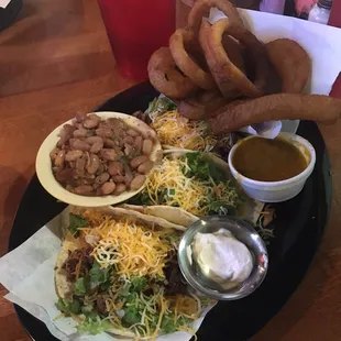 3 brisket tacos with two sides, pinto beans and onion rings.