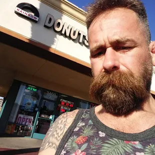 a bearded man in front of a donut shop