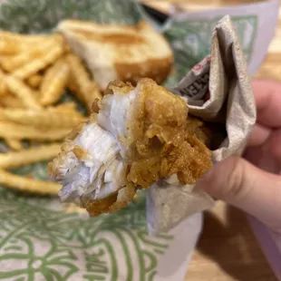 a hand holding a piece of fried chicken