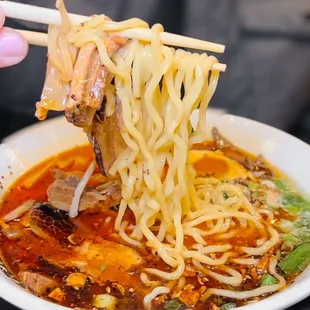 a person holding chopsticks over a bowl of ramen