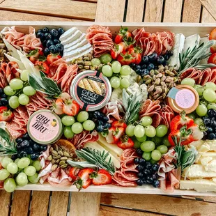 a platter of meats, cheese, grapes, and fruit