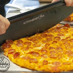 a person cutting a pepperoni pizza